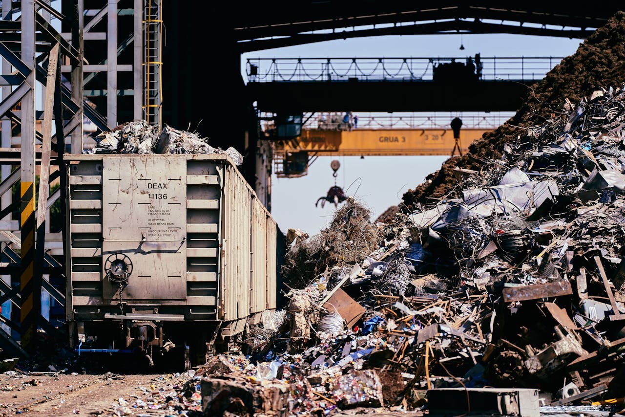 Home A dynamic industrial scene featuring a scrap yard with a train car and crane lifting debris.